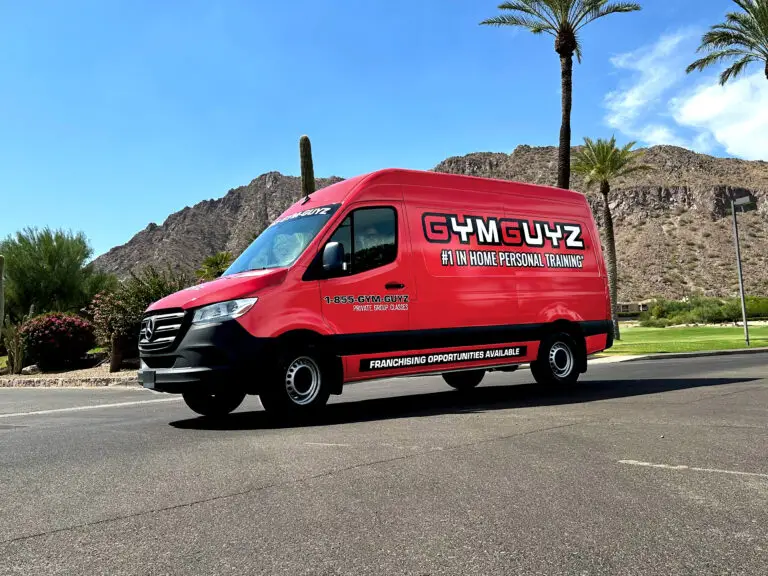 Red GYMGUYZ Mercedes Sprinter van with branded vehicle wrap parked outdoors, showcasing mobile in-home personal training and franchise opportunity messaging.