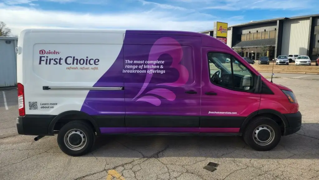 A van with a wrap on it for Daiohs USA that is pink and purple with people smiling with their coffee.